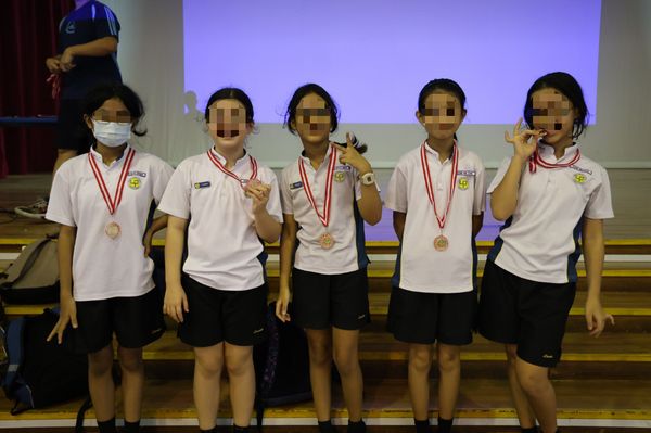 Five primary school girls from Lianhua Primary School smiling and holding their medals after the Inter-Class Games, celebrating their effort and teamwork.