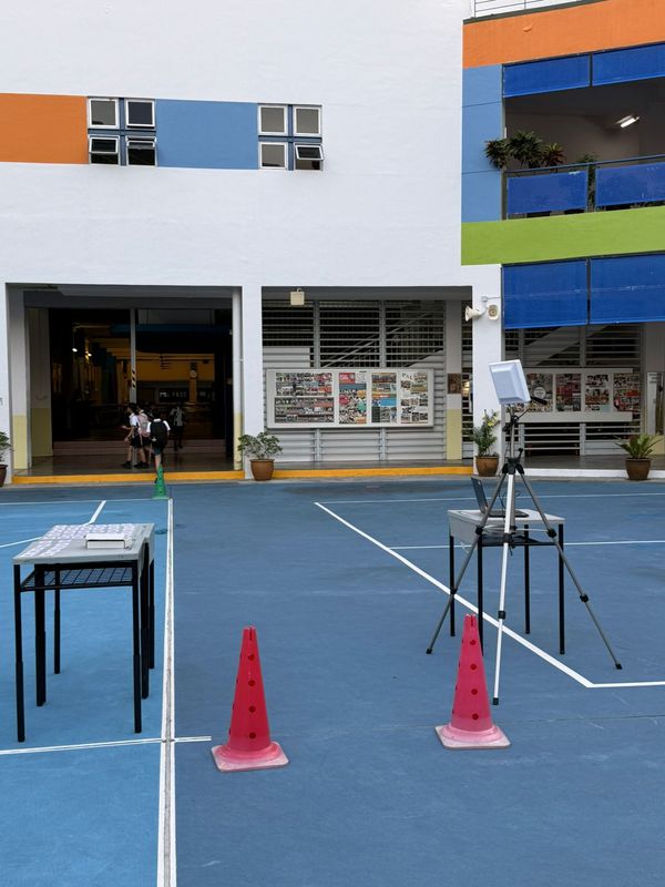 Two cones marking the single-file passing area between the numbered-card tables and a tripod-mounted RFID reader beside a laptop