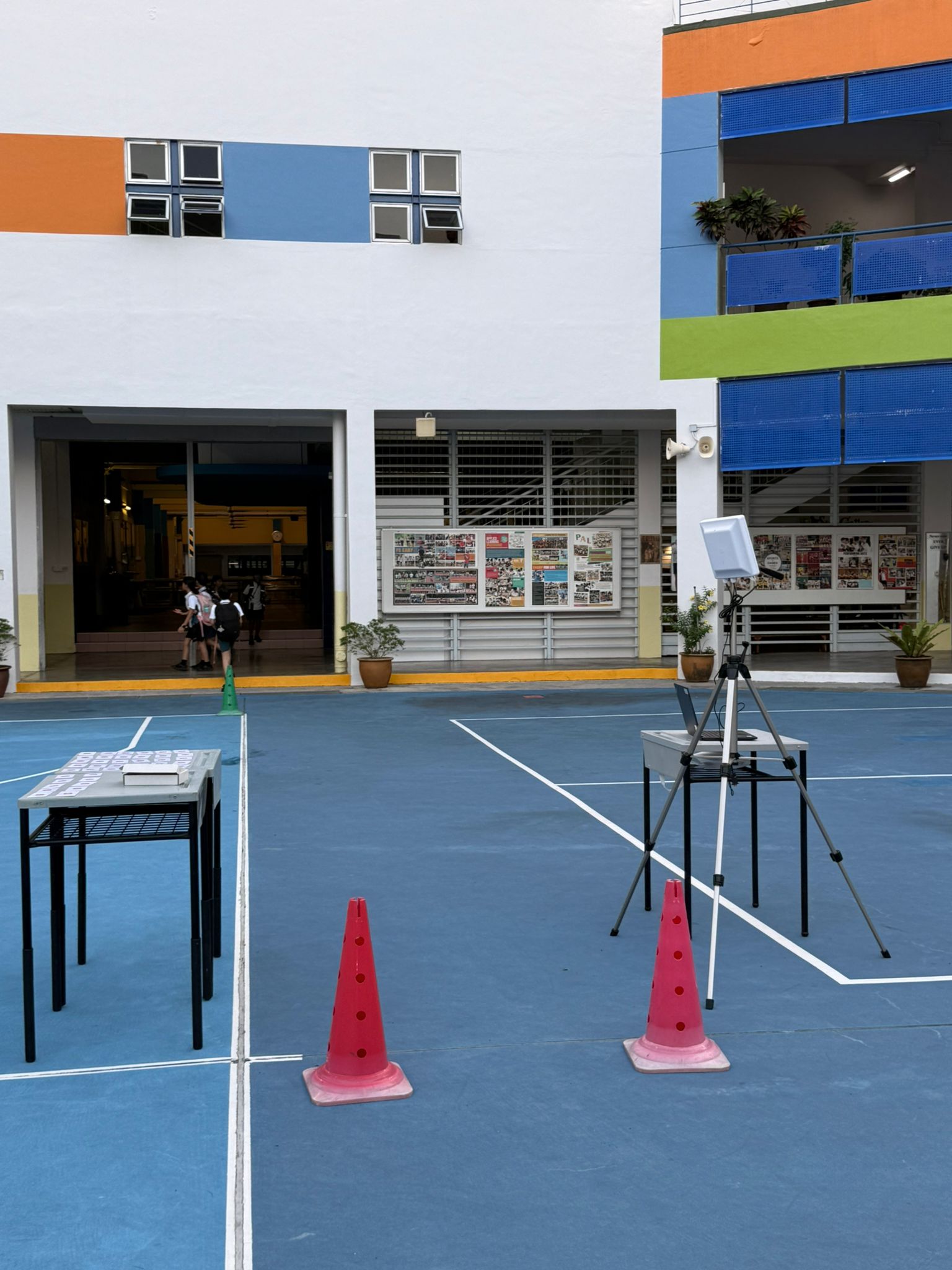 Cones marking a single-file passing area beside an RFID reader on a tripod and a teacher’s laptop